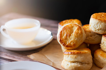 Close up homemade delicious dessert baked bread brown Traditional British Scones with blurred white cup of tea on wooden table and sunlight background.