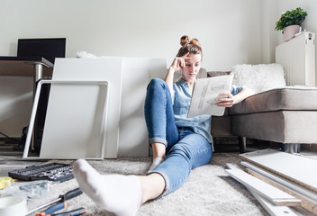 Concentrated young woman reading the instructions to assemble furniture at home in the living room