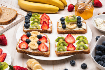 Sweet sandwiches with cream cheese and honey and fresh berries, strawberry, blueberry, kiwi, banana on a plate, wooden background. Top view, flat lay