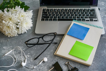 notebook with stickers, glasses, headphones and a laptop on the table on a gray background