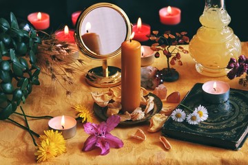 A yellow candle on a Litha midsummer Sabbat Solstice celebration altar filled with flowers, rose petals, dandelions, crystals, golden mirror, vintage book from 1837 representing a witch's grimoire.