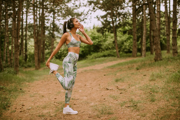 Young woman stretching and breathing fresh air in middle of forest while exercising