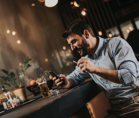 Man drinking beer, smoking cigarette and looking at mobile phone at the pub