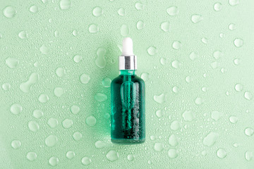 Moisturizing beauty essence in a dropper glass bottle on green background with water drops. Spa bathroom concept, copy space for your text