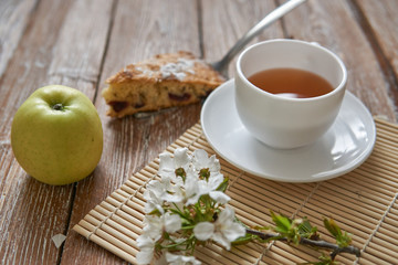 Homemade apple pie with cinnamon and cup of tea on wooden table.