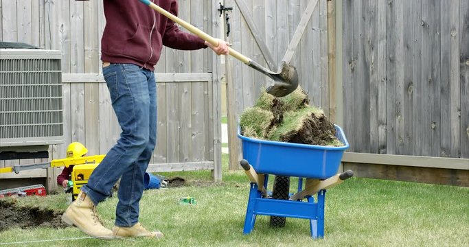 Father loading wheelbarrow as son plays with construction worker toys - wide shot