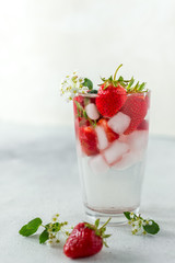 glass with a summer chilled clear carbonated drink, ice and strawberries. Refreshing coolness