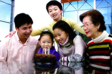 Girl sitting in front of her birthday cake with her family members surrounding her