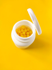 Pills of vitamin C in the opened white plastic container on bright yellow background.