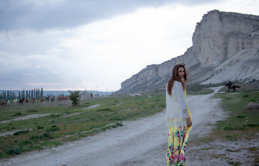 Beautiful woman dressed maxi dress, walking outdoor near horse paddock in the ranch against the...