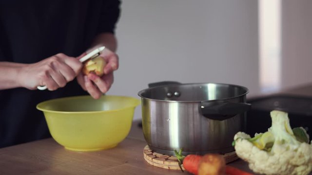 Millennial young woman cooking food, peeling potato at home kitchen. Circular economy, real food, organic waste