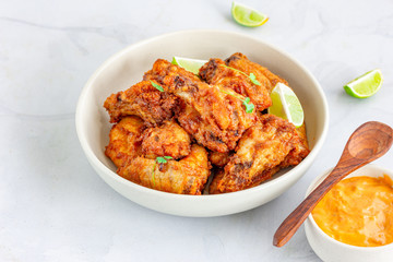 Oven Fried Crispy Chicken Wings in a White Bowl with Lemon and Dip Sauce on White Background