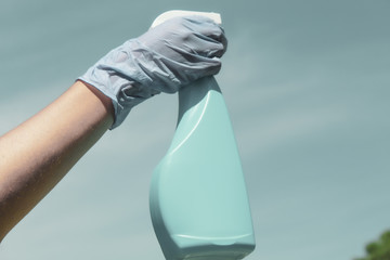 Mano humana con guante sanitario sujetando un pulverizador desinfectante para atacar bacterias y...
