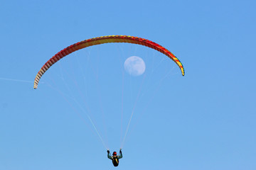 Paraglider flying wing in a blue sky with the moon	