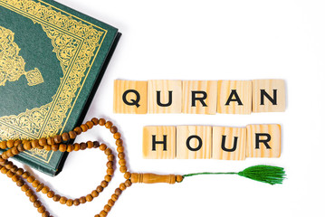 Word QURAN HOUR written on wooden cubes.Flat lay composition with Muslim prayer beads, Quran on isolated white background. Quran is public item for all Muslims.Islamic Concept.