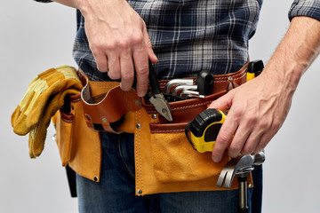 repair, construction and building - close up of male worker or builder with working tools on belt over grey background