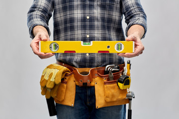 repair, construction and building - male worker or builder with level and working tools on belt over grey background