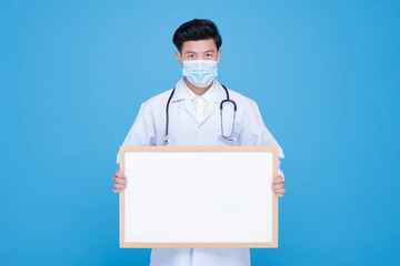 An Asian male doctor wears a surgical mask holding an empty whiteboard horizontally with both hands.