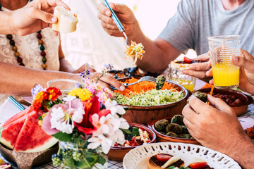 Family at lunch scene with unrecognizable caucasian mixed ages people eating and drinking together having fun for tradition or celebrating moments - close up of healthy coloured food on table