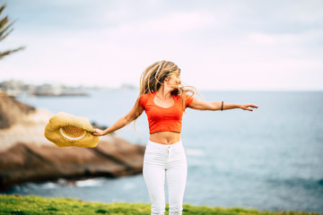 Happiness and joyful freedom people concept - young beautiful slim woman with long hair jump and dance in outdoor leisure activity alone with ocean and nature green meadow background