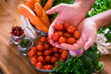 Close up of hands holding fresh and red coloured cherry tomatoes and various mix vegetables in backgraound cof healthy food nutrition concept lifestyle