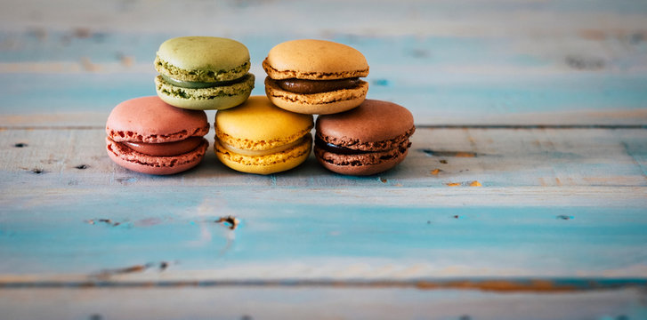 Close up of coloured and tasty hand made macarones cakes - sugar biscuits on a blue wooden trendy table - chocolatee and food energy concept