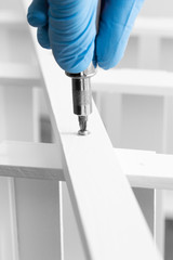 Man assembling a white flat pack ladder shelving unit with a screwdriver.  Flat pack assembly concept