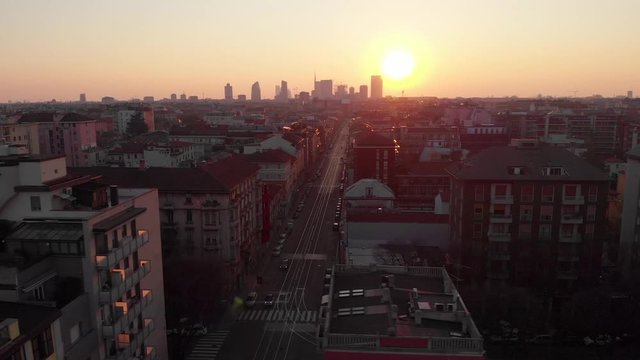 Drone aerial view of Milan skyline from above against colourful sunset over the city. Shot in Lambrate area during Coronavirus lockdown quarantine. Movement is sliding right.