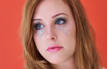 Pensive redheaded young woman glancing into the distance with beautiful gray eyes, wearing metallic glitter eye shadow makeup and pink lipgloss.