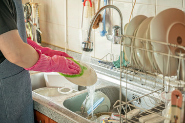 Middle-aged man's hand washing dishes in sink after meal.