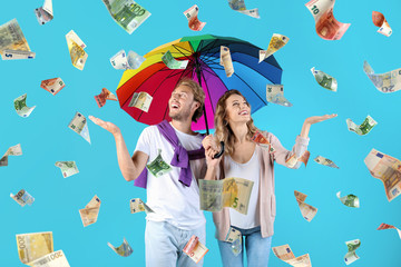 Couple with umbrella under money rain on color background