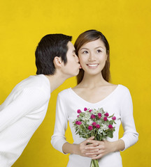 Woman getting a bouquet of flowers and a kiss from her boyfriend.