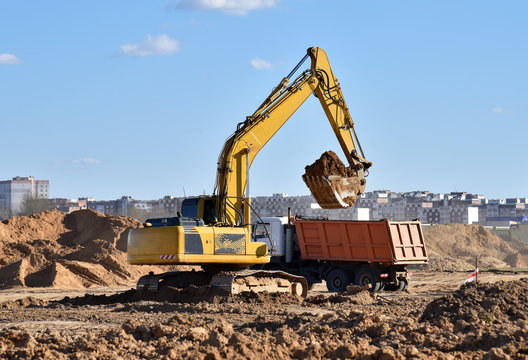 Excavator load the sand to the heavy dump truck on construction site. Backhoe digs the ground for the foundation and for laying sewer pipes. Renovation program. Buildings industry background