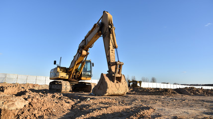 Fototapeta na wymiar Excavator working at construction site on earthworks. Backhoe digging building foundation. Paving out sewer line. Construction machinery for excavating, loading, lifting and hauling of cargo