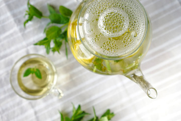 
teapot with herbal tea and water droplets on the lid with a cup and sprigs of fresh mint
