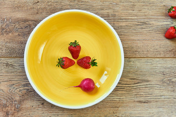 three strawberries and one radishon a yellow plate on a wooden tabletop