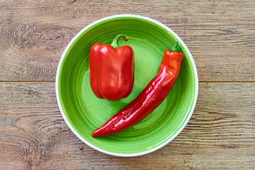thin and thick pods of different varieties of sweet pepper on a green plate on a wooden tabletop