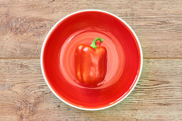 red pod of sweet bell pepper on a red plate on a wooden tabletop
