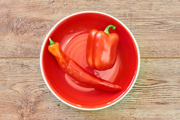 thin and thick pods of different varieties of sweet pepper on a red plate on a wooden tabletop