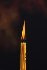 Two candles burning with the same merged great flame on a black background. Selective focus