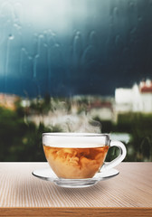 Glass cup with hot black tea and milk near window on rainy day