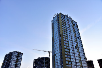 Fototapeta premium Tower cranes in action at construction site on sunset background. Thermal protection and Mineral wool insulation of the facade building. Installation double-glazed windows with frames