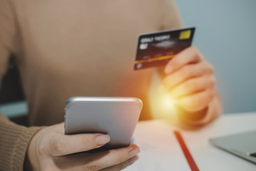 woman entering security code with digital mobile phone and paying with mock up credit card and laptop computer on desk at home office, shopping online, electronic pay and digital technology concept