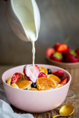 Mini oatmeal pancakes.Mini pancakes with blueberries and strawberries.Pancake porridge, mini pancakes in a bowl with milk and maple syrup.Dutch mini pancakes Milk is poured onto mini pancakes.