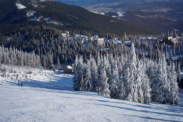 Snowy mountains and ski lifts. Skiers and snowboarders skiing downhill to village.