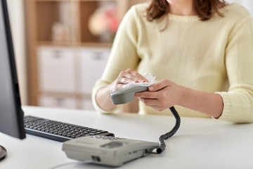 hygiene and disinfection concept - close up of woman hands cleaning desk phone with paper tissue