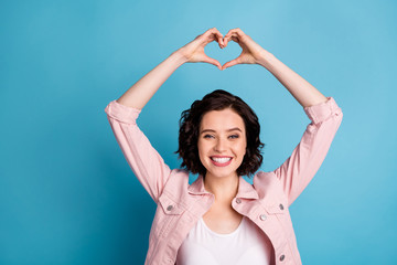 Fototapeta na wymiar Photo of beautiful cheerful lady short black hairdo hold arms above head making heart figure shape dreamer express feelings wear casual pink jacket isolated blue color background