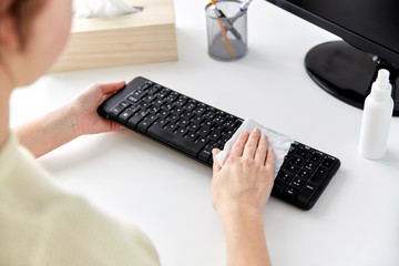 hygiene and disinfection concept - close up of woman hands cleaning computer keyboard with wet wipe