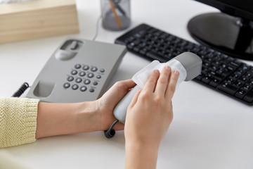 hygiene and disinfection concept - close up of woman hands cleaning desk phone with paper tissue