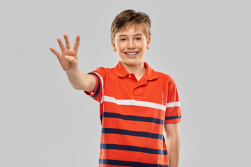 childhood, fashion and people concept - portrait of happy smiling boy in red polo t-shirt showing four fingers over grey background